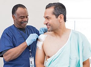 Healthcare provider checking dressings on man's shoulder.