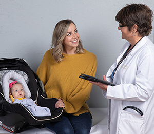 Una mujer con un bebé en un portabebés habla con una proveedora de atención médica.