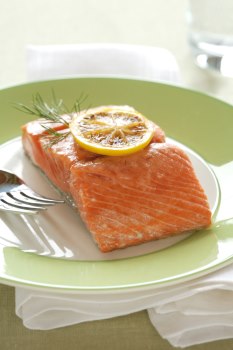 Plate containing a serving of salmon topped with a slice of lemon. A fork is resting to the side.